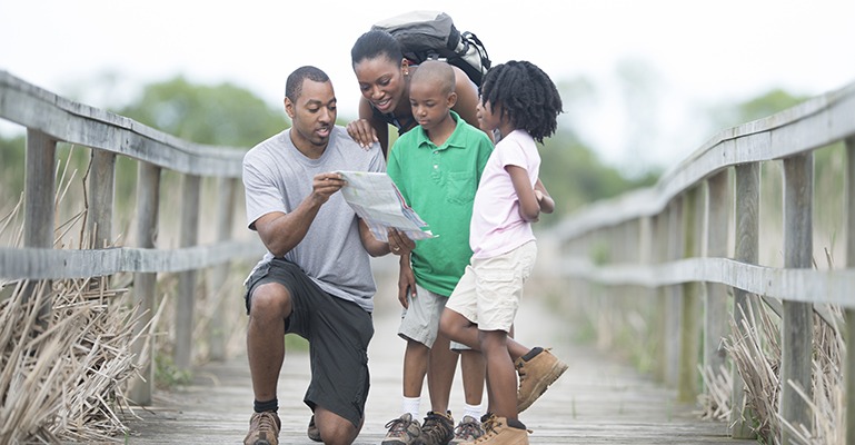 A family of four stops in the middle of an old, weathered pedestrian bridge to check their map.