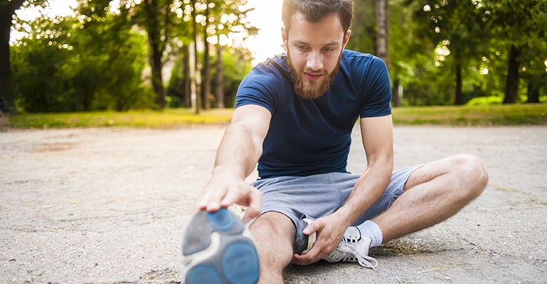 A young man stops in the middle of a run down an outdoor path to stretch his legs.