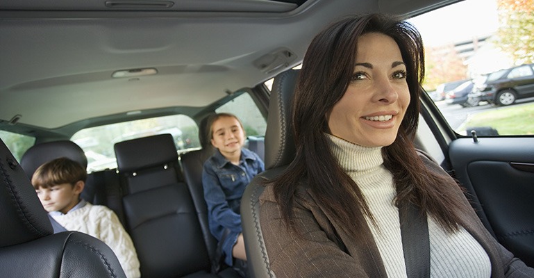 A mother drives down a suburban road with her son and daughter seated in the back of the car.