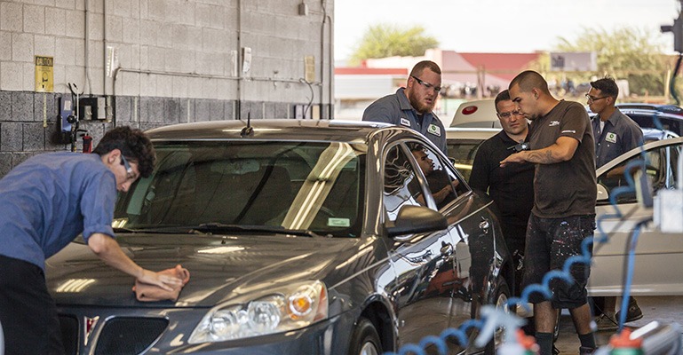 A group of workers at a body shop work on polishing a grey car.